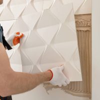 Installation of gypsum 3D panel. A worker is attaching the gypsum tile to the wall.