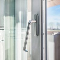 Closeup of PVC window with white metal frame and handle installed at house, view on blurred trees and sky. Household concepts.